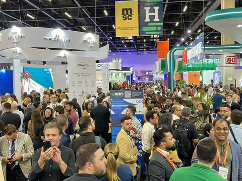Pavilhão de uma feira de logística e transporte marítimo, cheio de gente, com os estandes da MSC e da CMA CGM e faixas penduradas no teto