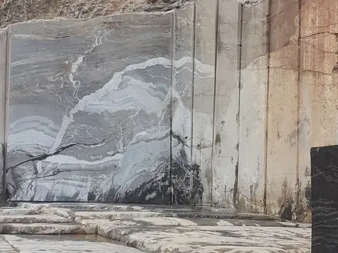 Paredão de rocha cortado em blocos numa pedreira, com veios brancos na pedra cinza e um bloco escuro à direita